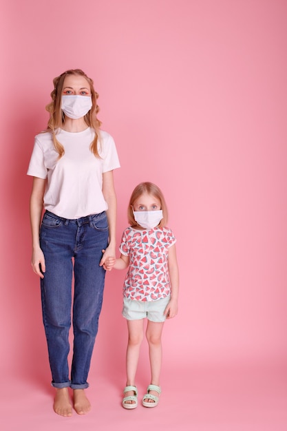 Mom and daughter in medical masks hold hands on pink surface