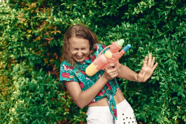 Mom and daughter in national Thai shirts shoot at each other with water pistols. Songkran Thai new year.