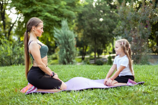 Mom and daughter play sports together on a mat in the park Motherhood Spending Time Mommy Trainer