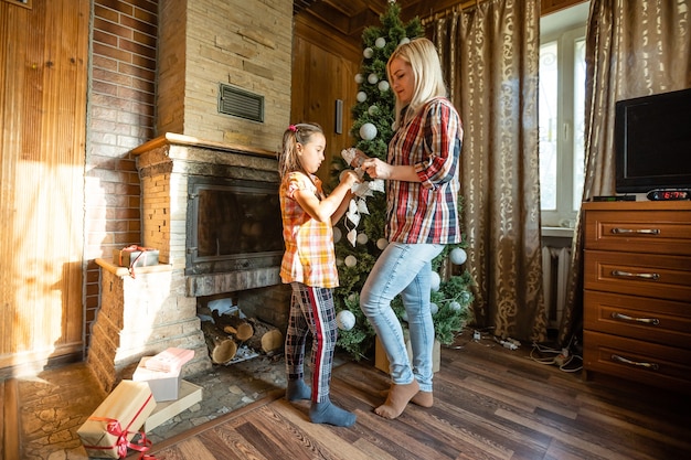 Mamma e figlia che giocano con le palle vicino all'albero di natale. regali, luci, palline sullo sfondo.