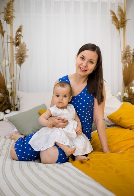 Mom and daughter sit on the bed and look at the camera in the bedroom