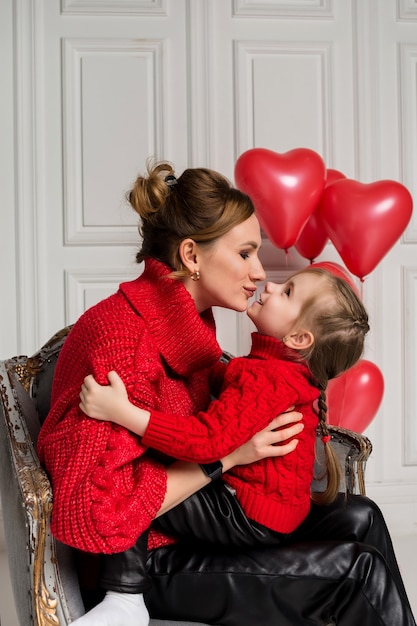 Mom and daughter sit in a chair and kiss on white