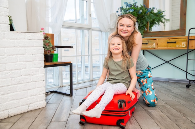 mom and daughter sitting astride a red suitcase on vacation and smiling vacation concept. 