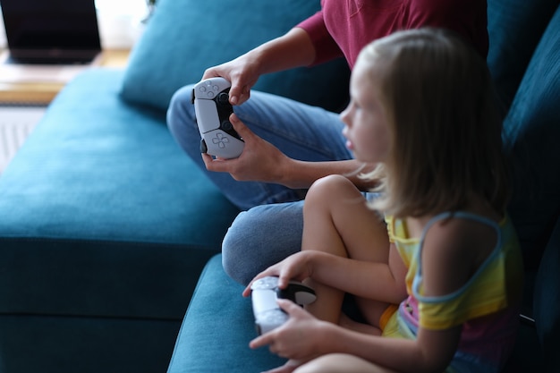 Mom and daughter sitting on couch and holding computer joysticks closeup