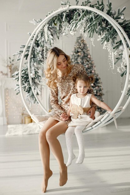 Mom and daughter sitting on round swing near Christmas tree