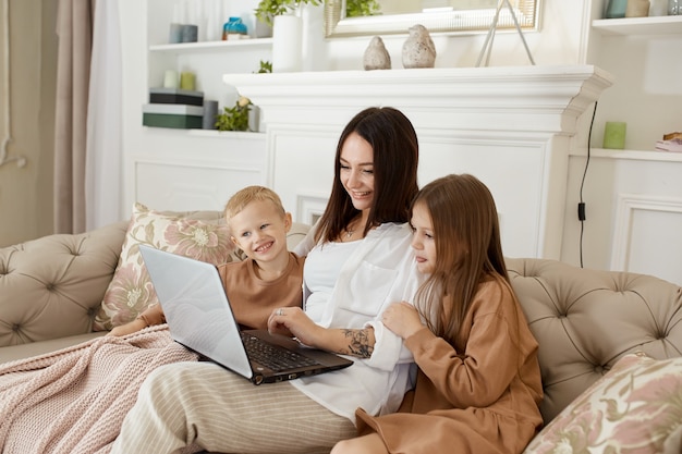 ママの娘と息子はラップトップで遊ぶ。家族のレクリエーションとレジャー