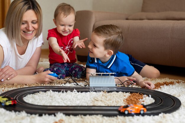 Mom and daughter and son play racing on the carpet.