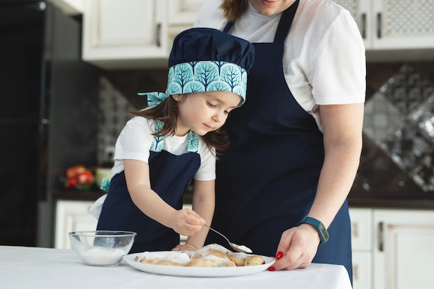 Mom and daughter sprinkle cookies with powdered sugar