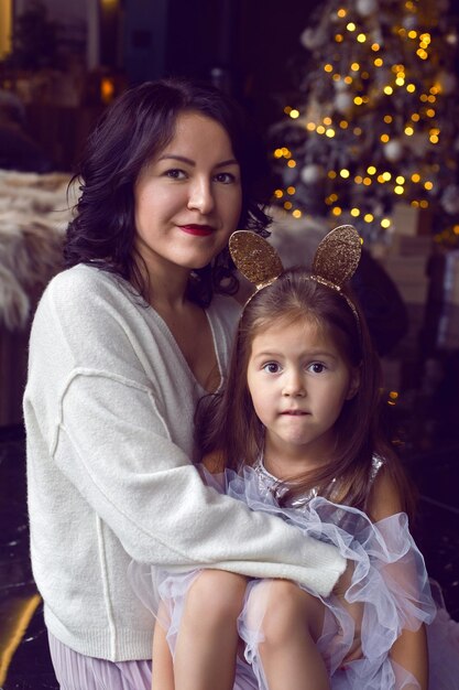 Mom and daughter standing at the christmas tree in the studio at christmas