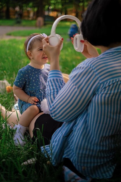 Mom and daughter in summer dresses listening to music in headphones face to face against