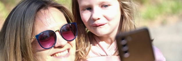 Mom and daughter take selfie on phone on sunny day family photos and summer walks concept