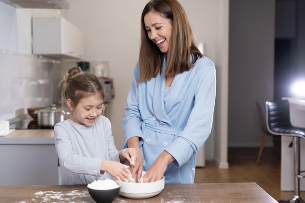 Mom and daughter together in the kitchen knead dough in a bowl Cooking concept together at home Copy space