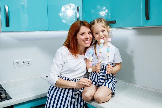 Mom and daughter in the turquoise kitchen are playing with marshmallows. Lovely family relationships. Happy family concept