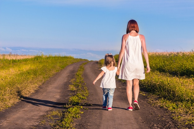 Mom and daughter walk along a country road along a wheat field on a warm summer day