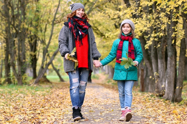 Mom and daughter on a walk in the autumn park during the fall of the fall