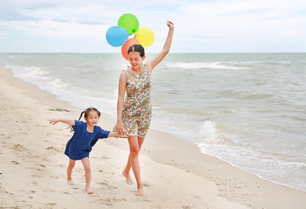 Mom and daughter walking on beach with colorful balloons in mother hand