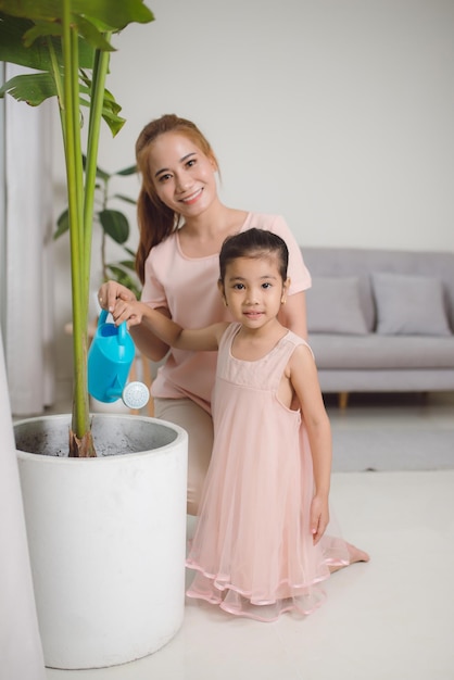 Photo mom and daughter watering plants in the apartment