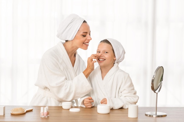 Mom and daughter wearing bathrobes making beauty routine at home