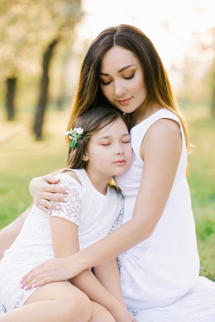 Mom and daughter in white dresses on a picnic in summer