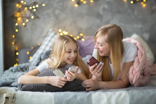 Mamma e figlia con i telefoni che ridono abbracciandosi