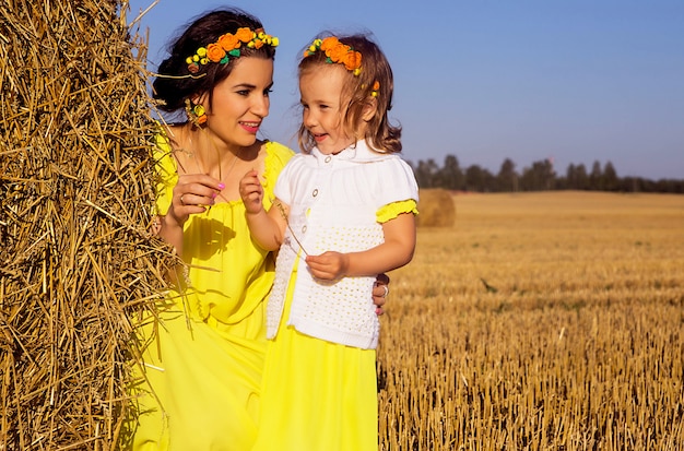 Mom and daughter in yellow dresses on a hay field