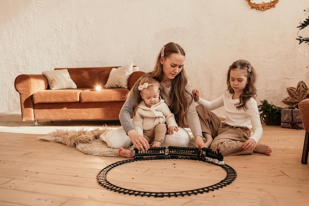 Mom and daughters are sitting on the carpet in the room and playing with the railroad with the train