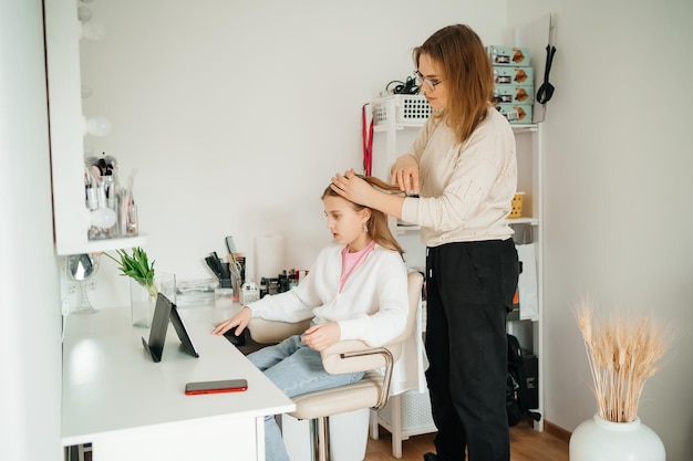 Photo mom does her daughter hair a teenager uses a tablet