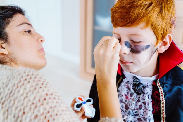 Mom doing vampire makeup to little kid at home for Halloween spooky costume party