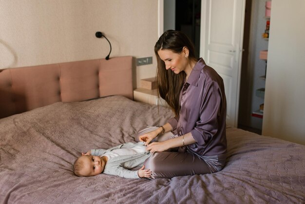 Mom dresses cute little baby boy in a jumpsuit Happy motherhood