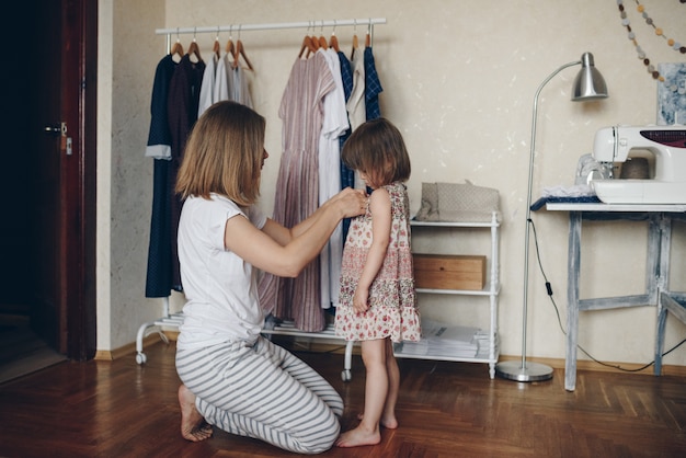 Photo mom dresses her daughter in a dress. morning.