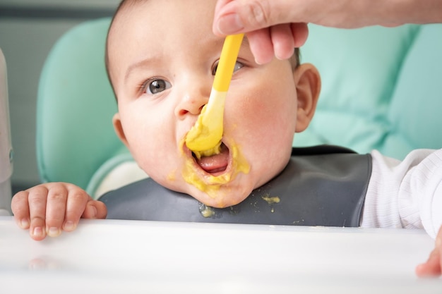 ママは子供の食事のテーブルで野菜のピューレのスプーンで赤ちゃんを養います 赤ちゃんの食欲 健康的な栄養 補完食品の紹介 Copyspace モックアップ