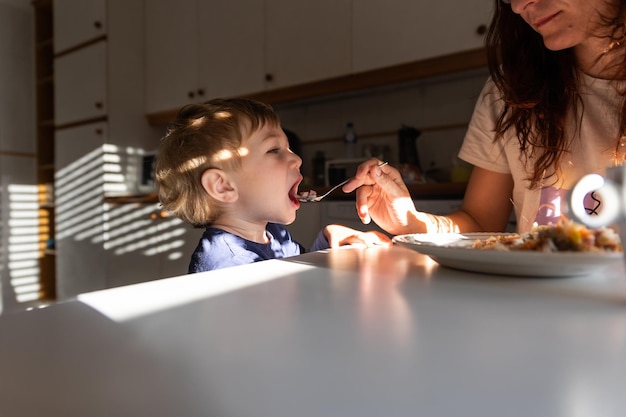 Mom feeds her little boy with a spoon in the kitchen