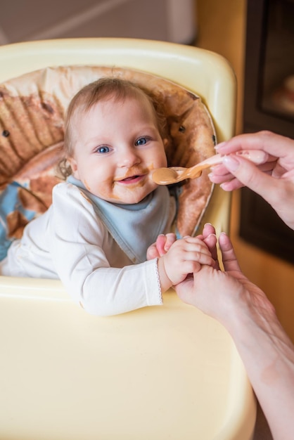 Mom feeds her little daughter fruit puree from a spoon First food
