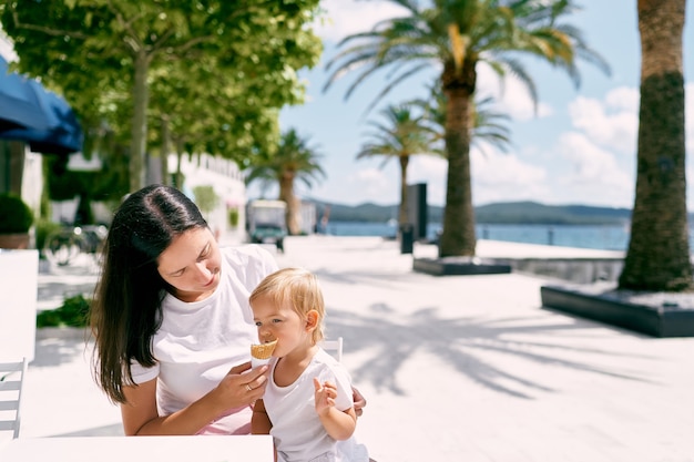 Mom feeds little girl ice cream in a cafe on the beach