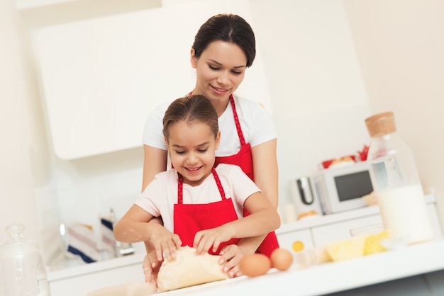 Mamma e ragazza preparano la pasta in grembiuli rossi.