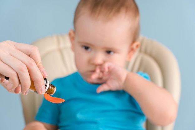 Mom gives toddler 12-17 months medicinal syrup on a spoon, selective focus