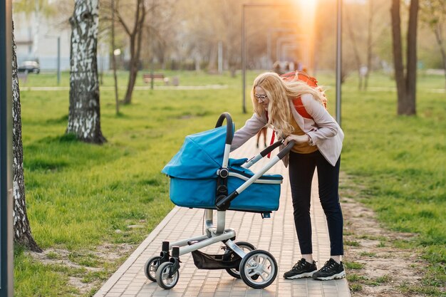 Photo mom in glasses walks with a stroller in the park