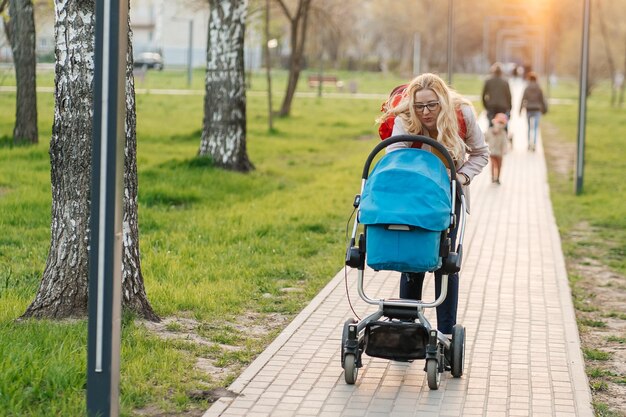 Mom in glasses walks with a stroller in the park