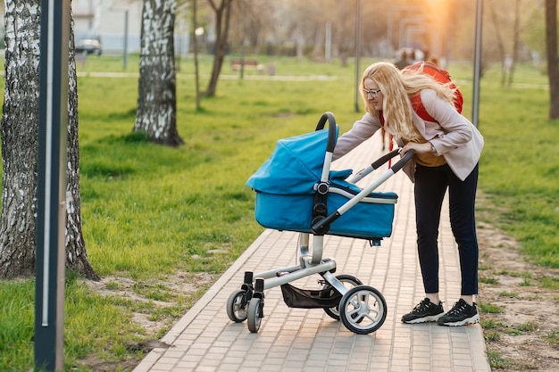 Foto mamma con gli occhiali cammina con un passeggino nel parco