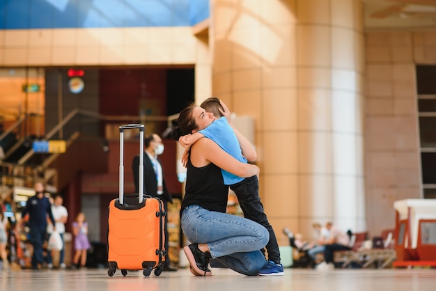 Mom gretting her son at the airport with a suitcase