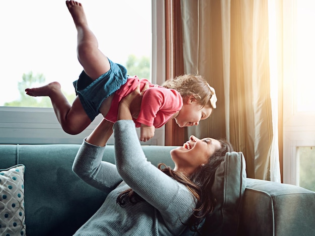 Mom happy and lifting girl on sofa in home living room and relax bonding and quality time together or mother love and family happiness Child mommy and playing game on couch in house with smile