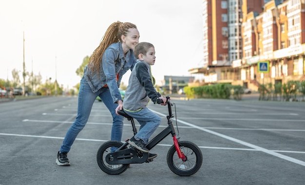 Mom helps a child boy learn to ride a twowheeled bicycle in the park A pleasant children's summer sports vacation