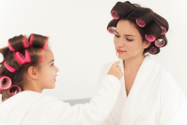 Mom helps the girl to make up and look beautiful.