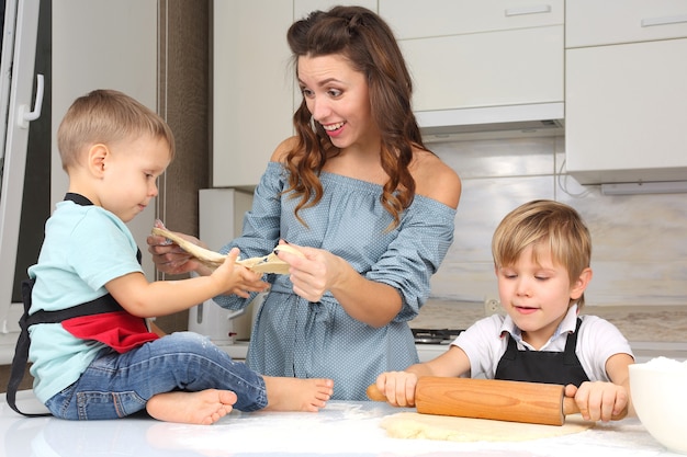 Mom helps young sons knead the dough on the kitchen table
