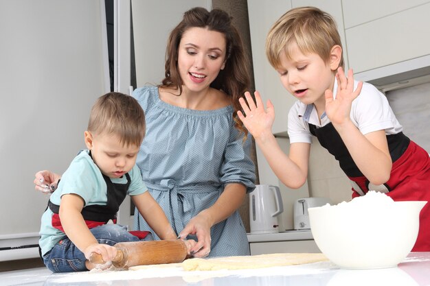 Mom helps young sons knead the dough on the kitchen table