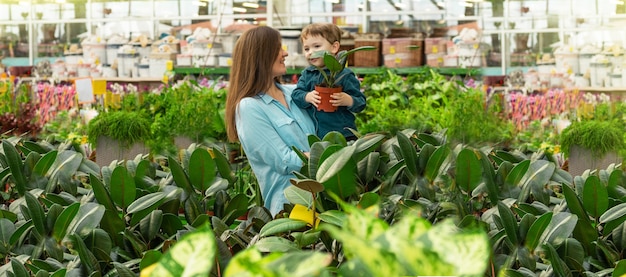 植物屋のママと彼女の男の子は植物を選びます。温室でのガーデニング。植物園、花の栽培、園芸産業のコンセプト