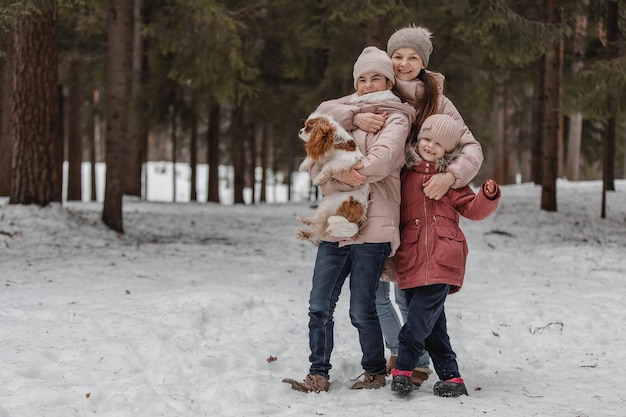 Mom and her daughters are playing in a snowy forest with their dog