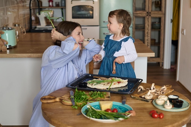 Mom and her little daughter cook pizza together in the kitchen The concept of a happy family