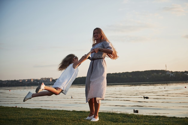 Photo mom and her little daughter play on the grass near the lake.