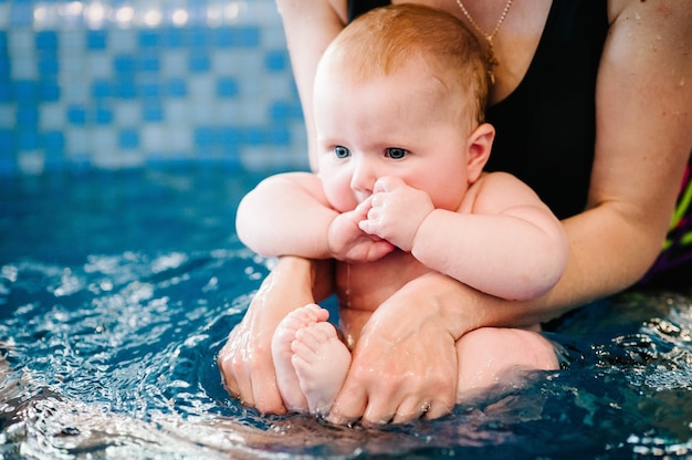 ママはダイビングの準備をしている子供を抱きしめています。若い母親、水泳インストラクター、プールで幸せな女の子。